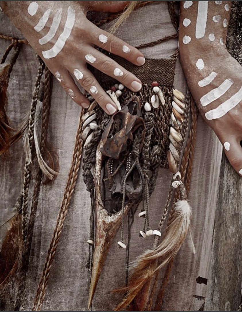 Painted hands resting on a medicine bundle of cowrie shells, bone, feathers and braided cord
